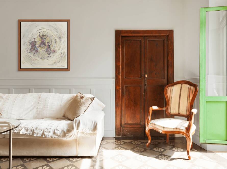 Framed artwork of three Hasidic men dancing in a golden circle, hanging above a modern white sofa beside a vintage wooden door and sunlit window.