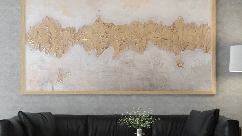 Chaya Koritz's golden abstract painting hangs above a dark gray couch in a modern room.